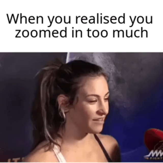 This meme has text at the top reading "When you realised you zoomed in too much" above a cropped still from an MMA sports interview. The still shows real female MMA fighter Miesha Tate wearing a sports bra, facing slightly right with a small amused smile. A forced perspective from the close zoom makes a curved grey shape in the background behind her head align perfectly with her face, creating a visual illusion that she has a phallic-shaped nose. The joke refers to the awkward, suggestive effect of an overly close or intentionally framed zoom shot, implying the cameraman set up the shot deliberately for this humorous suggestive result.