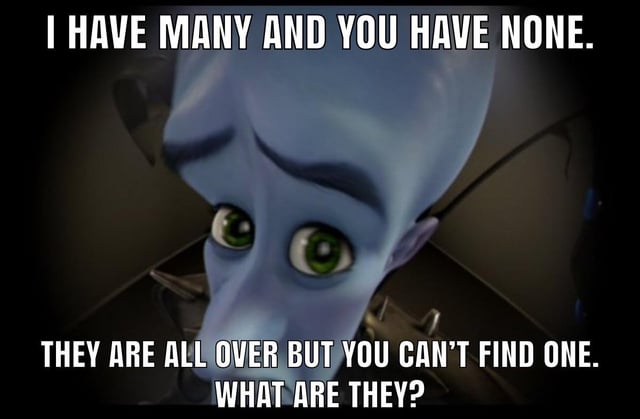 This is a single-panel text-overlay meme using a still frame of the animated character Megamind, a blue-skinned big-headed alien with large green eyes, who looks directly at the viewer with a playful, slightly smug wide-eyed expression. Overlaid bold white text presents a riddle: top text reads 'I HAVE MANY AND YOU HAVE NONE.', middle bottom text reads 'THEY ARE ALL OVER BUT YOU CAN'T FIND ONE.', followed by the question 'WHAT ARE THEY?'. The common intended answer to the riddle is 'friends', which forms the joke, leaning into relatable humor about people struggling with loneliness or difficulty making friends.