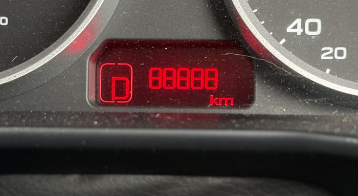 A close-up photograph of a car's dashboard instrument cluster, focusing on the odometer display. The odometer shows a mileage of 88888 km in bright red digital numbers. To the left of the mileage, there is a 'D' indicator, likely representing the Drive gear. The surrounding dashboard area is dark, with parts of the speedometer visible on the right, showing increments up to 40 (units not specified). The surface has minor dust particles, indicating a real-world, unstaged setting.