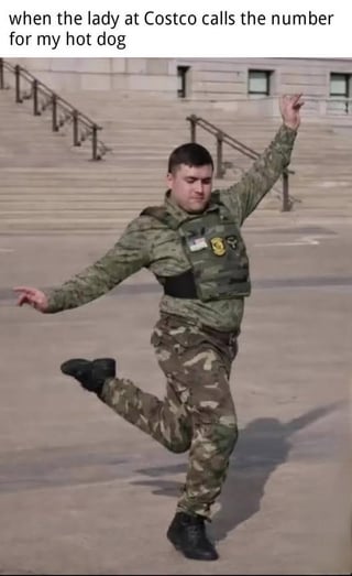 This meme pairs a photograph of a real person in military camouflage and body armor, striking an energetic, joyful dance pose (one leg lifted, arms outstretched in a celebratory manner) with the top text: *when the lady at Costco calls the number for my hot dog*. The humor stems from the stark contrast between the subject's serious military attire and their over-the-top, giddy reaction to the mundane but beloved experience of getting a Costco hot dog, a popular, low-cost item at the warehouse chain. It exaggerates the relatable excitement of receiving a highly anticipated, simple treat.