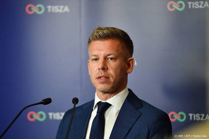 This is a photograph of Hungarian opposition politician Péter Magyar (referred to as JD in the original post title) giving a speech at an official TISZA party press conference. He stands behind a podium with two microphones, in front of a blue repeating branded backdrop for his political party TISZA. The post is a celebratory reaction to a recent political milestone or win achieved by the politician.