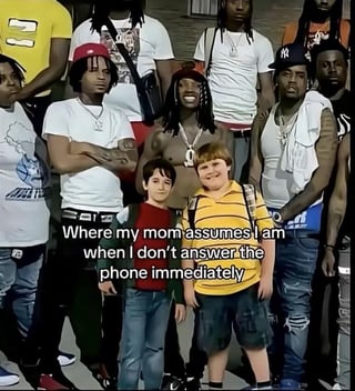 This is an absurdist relatable meme. The base image displays two young preteen boys standing in front of a large group of adult Black men dressed in casual streetwear and jewelry, which fits the stereotypical cultural image of a potentially unsafe street group. Overlaid text on the image reads: 'Where my mom assumes I am when I don't answer the phone immediately', which pokes fun at common parental overanxiety where parents assume their children are in dangerous situations if they do not respond to communications right away. The meme's punchline in the title adds that the child is actually in North Korea, a location widely stereotyped as far more dangerous and isolated than the scenario the mother imagines, creating a layered comedic contrast between the minor perceived danger the mother fears and the far more extreme real situation.