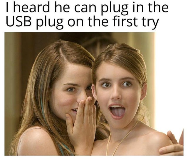 The meme features two young women standing close together. The woman on the left has long brown hair, is cupping her hand to her mouth, and appears to be whispering into the ear of the woman on the right. The woman on the right has shorter brown hair, wide eyes, and an open mouth, displaying a shocked or surprised expression. Above them is a text overlay that reads, "I heard he can plug in the USB plug on the first try." The humor arises from the relatable frustration of struggling to insert a USB connector correctly on the first attempt, framed as an impressive achievement that elicits shock.