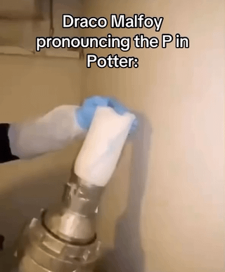 The image features a close-up photograph of a hand wearing a blue glove holding a white cylindrical object (resembling a plunger) pressed against a beige wall. At the top of the image, there is bold white text that reads: 'Draco Malfoy pronouncing the P in Potter:'. The meme relies on a pun, humorously implying that Draco Malfoy (a character from the Harry Potter series known for his haughty demeanor and disdain for Harry Potter) would emphasize the 'P' sound in 'Potter' in an exaggerated manner, with the visual of the plunger (associated with the verb 'plunge') reinforcing the phonetic joke of the hard 'P' pronunciation.