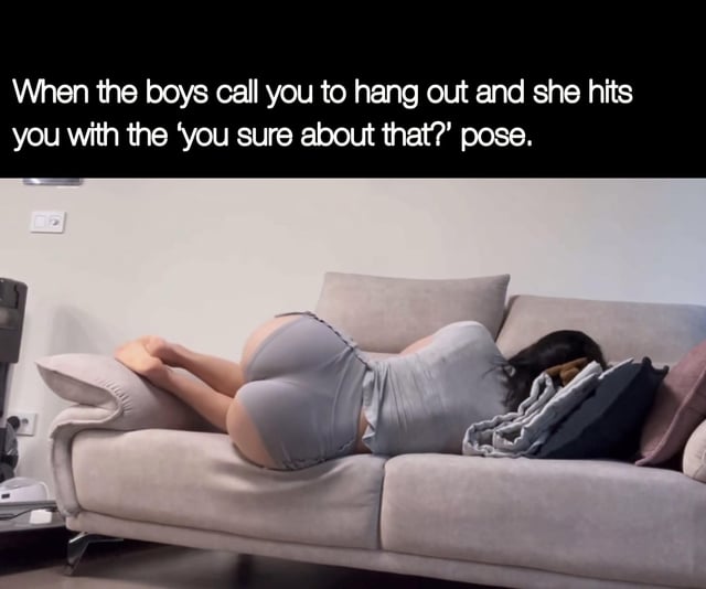 A meme featuring a photograph of a woman lying on her stomach on a light gray sofa, wearing form-fitting gray loungewear (shorts and a top). Her legs are bent with feet resting on the couch arm, and her head is resting on a pile of pillows, obscuring her face. Above the image is a text overlay that reads: 'When the boys call you to hang out and she hits you with the 'you sure about that?' pose.' The humor lies in the suggestive implication that the woman's posture is intended to persuade the viewer to choose staying with her over going out with friends.