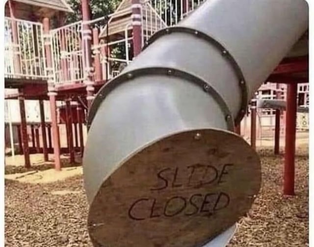 The image depicts a playground slide with a metal tube structure. One end of the slide is covered by a circular wooden board, on which the handwritten text 'SLIDE CLOSED' is visible. The background shows other playground equipment with red support beams and a ground covered in wood chips. The humor lies in the implication that closing only one end of the slide (likely the bottom) is ineffective, as the other end (top) might still be accessible, prompting the original title's joke about placing the same sign on the other opening.