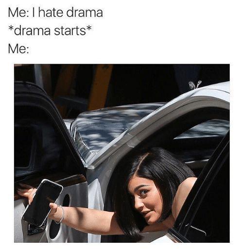 A meme consisting of top text and a bottom image. The top text reads: 'Me: I hate drama *drama starts* Me:'. Below is a photograph of a woman with dark hair leaning out of a car window, holding a smartphone in her right hand, looking intently to her side with a curious and eager expression. The meme humorously portrays the irony of someone claiming to dislike drama but becoming immediately interested when it occurs.