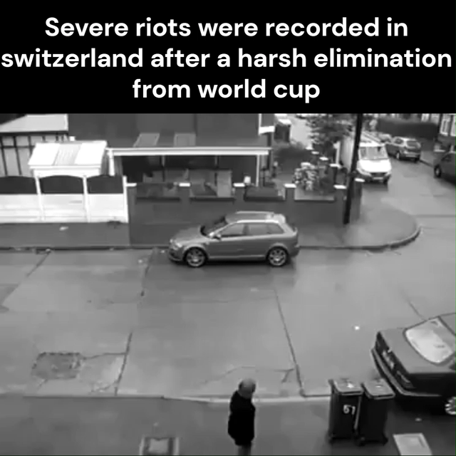 This is a satirical meme that uses extreme contrast for humor. The top text makes a dramatic claim that severe riots broke out in Switzerland after the country was eliminated from the FIFA World Cup, but the accompanying CCTV footage shows an entirely quiet, peaceful residential street with only one person walking slowly, no property damage, no crowds, and no signs of unrest whatsoever. The joke relies on the widespread cultural stereotype of Switzerland being an extremely orderly, peaceful, low-disruption country, implying that even the worst possible "riots" in Switzerland are indistinguishable from normal, boring daily life, while also mocking overblown media coverage of post-World Cup unrest in other nations.