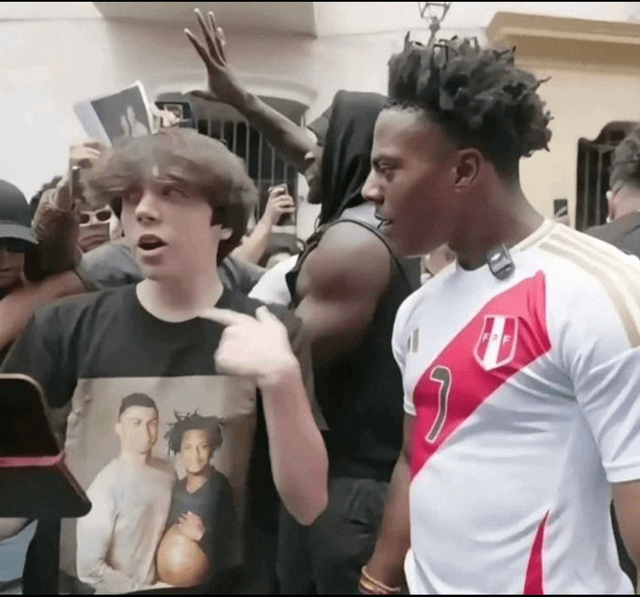 This candid photograph captures popular internet streamer IShowSpeed (Darren Watkins Jr.) standing beside a young fan at a public meetup. The fan is excitedly pointing at the print on his t-shirt, which features an edited image of IShowSpeed alongside his idol, famous footballer Cristiano Ronaldo. A crowd of onlookers in the background are holding up phones to record the interaction, emphasizing the public, fan-facing nature of the event. The meme is framed as a wholesome, positive 'win' for Speed, referencing his well-documented public admiration for Ronaldo.