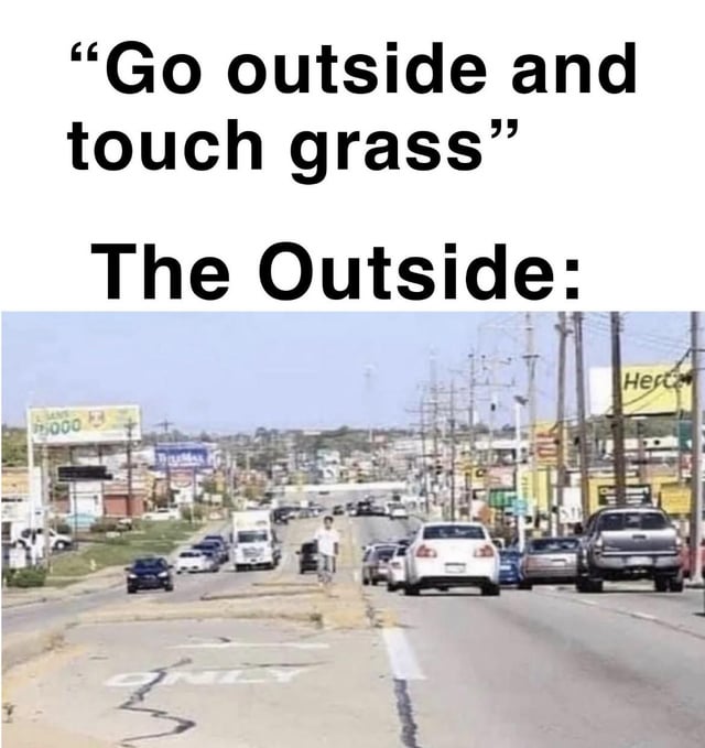 This meme opens with the common internet phrase "Go outside and touch grass", a saying used to suggest people who spend excessive time online should go experience real life. Below this text is a photo of a busy, heavily paved suburban/commercial road in a car-dependent area, with traffic on both sides, cracked asphalt, utility poles, billboards and storefronts lining the street, with almost no visible green grass. The joke highlights the disconnect between the idyllic, nature-filled idea of 'going outside' implied by the phrase, and the unappealing, hot, concrete-heavy actual outside environment many people encounter, especially during summer months.
