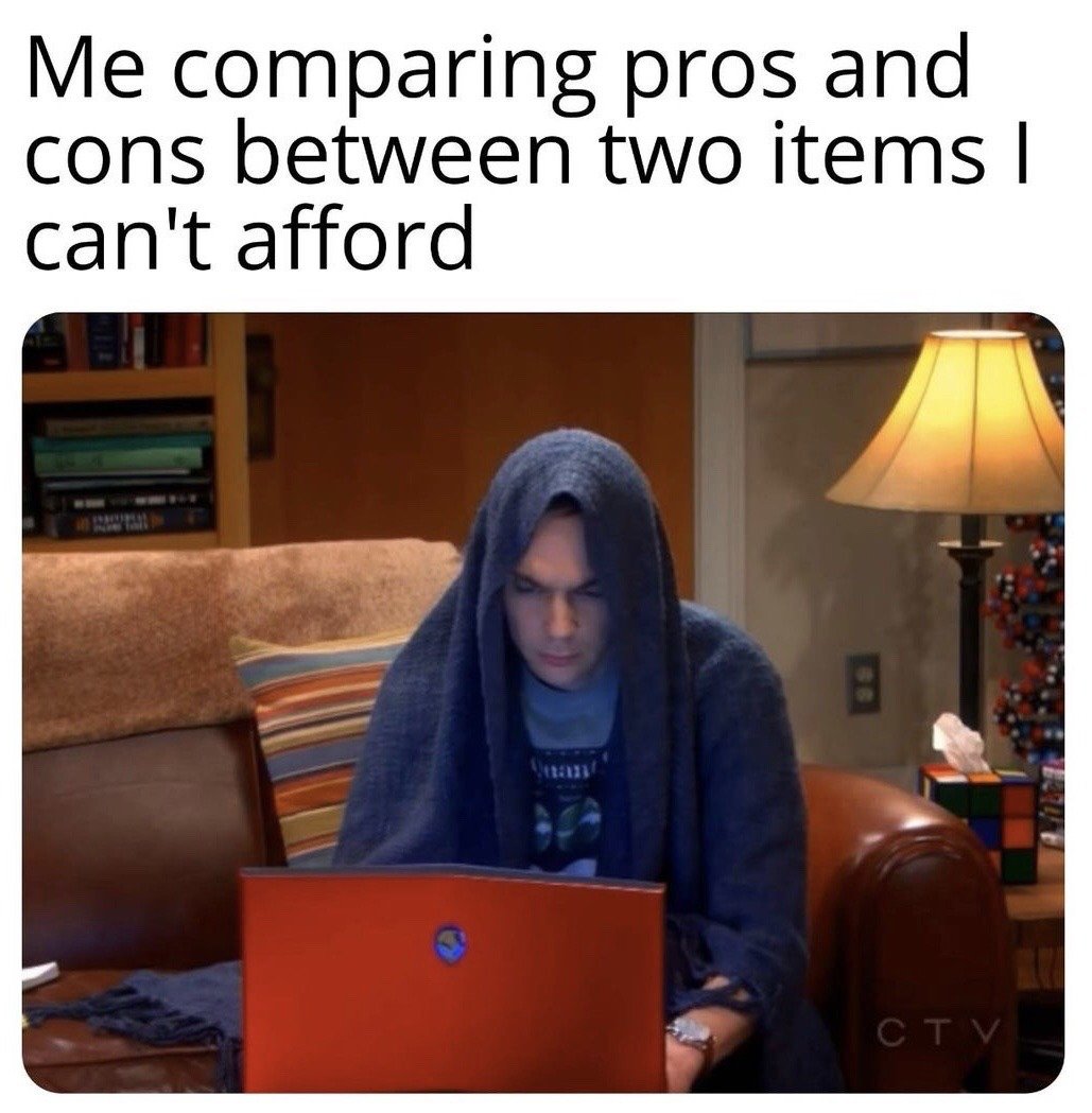 This is a relatable humor meme. The top text reads 'Me comparing pros and cons between two items I can't afford'. Below the text is a still frame of Sheldon Cooper from the sitcom The Big Bang Theory, sitting on a brown leather couch in his apartment with a dark blue blanket draped over his head, staring intensely and seriously at his red laptop. The background includes a striped couch pillow, a bookshelf, a table lamp, and a Rubik's cube themed tissue box. The joke highlights the common, frivolous habit of spending significant time researching and comparing high-cost products that are completely outside of one's budget, despite having no ability to purchase either option.