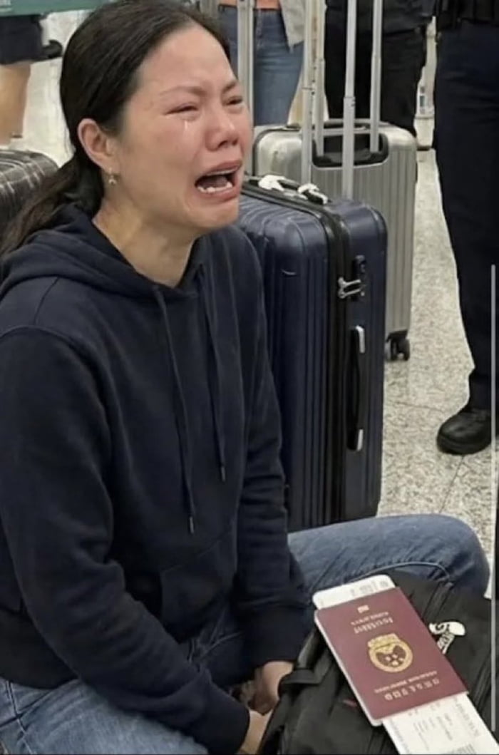 The image shows an East Asian woman sitting on the tiled floor of what appears to be an airport terminal, visibly sobbing heavily with tears streaming down her face and her mouth open in distress. She is dressed in a dark navy hoodie and blue jeans. Multiple rolling suitcases are placed behind her, and a People's Republic of China passport with attached boarding passes rests on a black bag next to her legs. The accompanying context for the meme states this woman, who was living in Taiwan, was issued a deportation order by Taiwanese authorities after posting online content supporting the annexation of Taiwan to China, with the original post making a sarcastic joke that her visible tears are tears of joy at being sent back to China.
