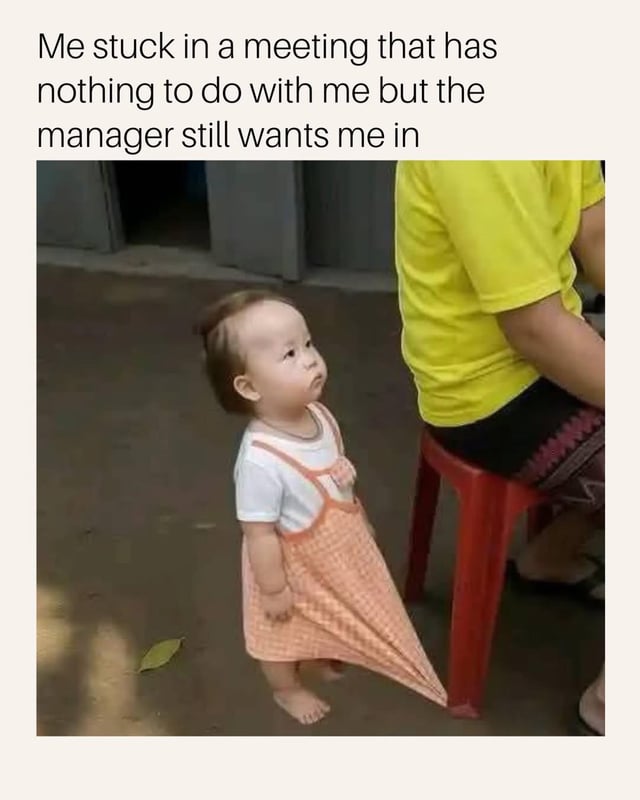 This is a relatable workplace humor meme. Text at the top of the image reads 'Me stuck in a meeting that has nothing to do with me but the manager still wants me in'. Below the text is a viral photo of a young toddler girl wearing a white t-shirt under a peach checkered dress, standing barefoot outdoors. The hem of her dress is caught under the leg of a red plastic stool where an adult in a bright yellow t-shirt is sitting, so the toddler is trapped standing in place with a bored, unimpressed, annoyed expression on her face, perfectly illustrating the relatable frustration of being forced to stay in a pointless, irrelevant work meeting you have no stake in.