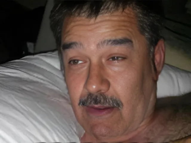 A meme image featuring a real man lying in bed on a white pillow, captured mid-reaction with a groggy, startled, and half-awake expression. His head is turned to the side, as if responding to an unexpected noise. The humor stems from the contrast between his peaceful early-morning state and the implied urgency of the scenario described in the title: being abruptly awakened at 6 am by loud knocking from Delta Force (an elite military unit), creating a comedic exaggeration of an unexpected early-morning interruption.