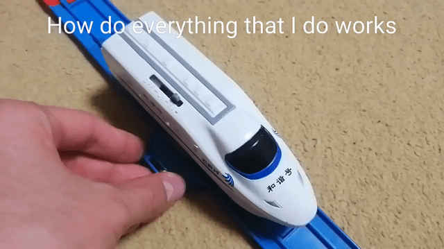 A photograph showing a close-up of a white toy train model with the Chinese characters '和谐号' (Hexie Hao, referring to China Railways high-speed trains) on its front, positioned on a blue plastic track. A human hand is gently holding the train from the side. At the top of the image, there is an overlaid text that reads 'How do everything that I do works', which contains a grammatical error ('do' instead of 'does'), contributing to the meme's lighthearted and humorous tone. The background consists of a beige carpeted surface, creating a casual, everyday setting.