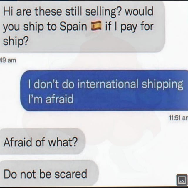 This is a screenshot of a text message conversation between a potential buyer and a seller. The buyer first asks if the listed items are still for sale, and inquires if the seller will ship items to Spain (accompanied by the Spanish flag emoji) if the buyer covers shipping costs. The seller politely declines, writing 'I don't do international shipping I'm afraid'. The humor comes from the buyer's complete misunderstanding of the common polite English set phrase 'I'm afraid' which is used to soften bad news: they interpret it literally to mean the seller is scared, so they reply asking 'Afraid of what?' followed by 'Do not be scared' to reassure the seller.