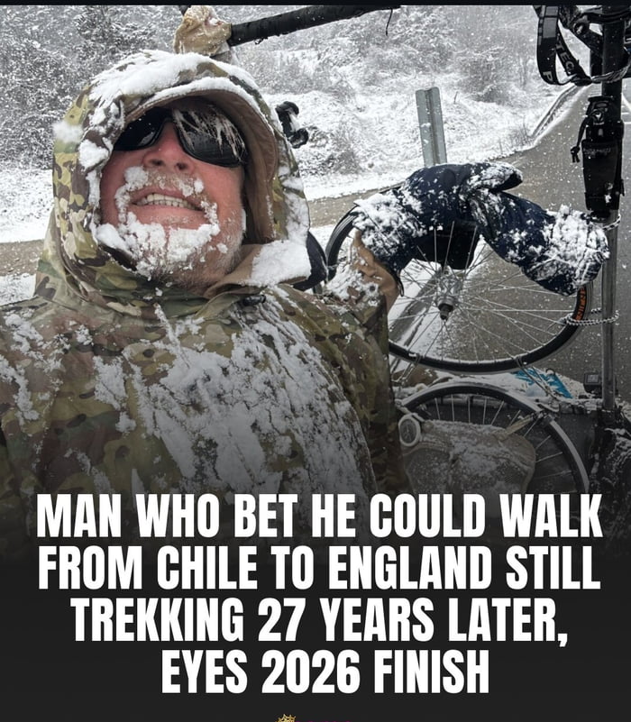 The image features a smiling adult man wearing a camouflage hooded jacket and snow-flecked sunglasses, completely covered in accumulated snow on his face, clothes, and hood. He is posing for a photo next to his bicycle on a roadside during active snowfall, with snow-covered hills visible in the background. Large white text overlaid at the bottom of the image reads: "MAN WHO BET HE COULD WALK FROM CHILE TO ENGLAND STILL TREKKING 27 YEARS LATER, EYES 2026 FINISH". The post leans into humor, prompting viewers to wonder how large the bet was that motivated this man to commit to a decades-long, extremely harsh cross-continental trek.
