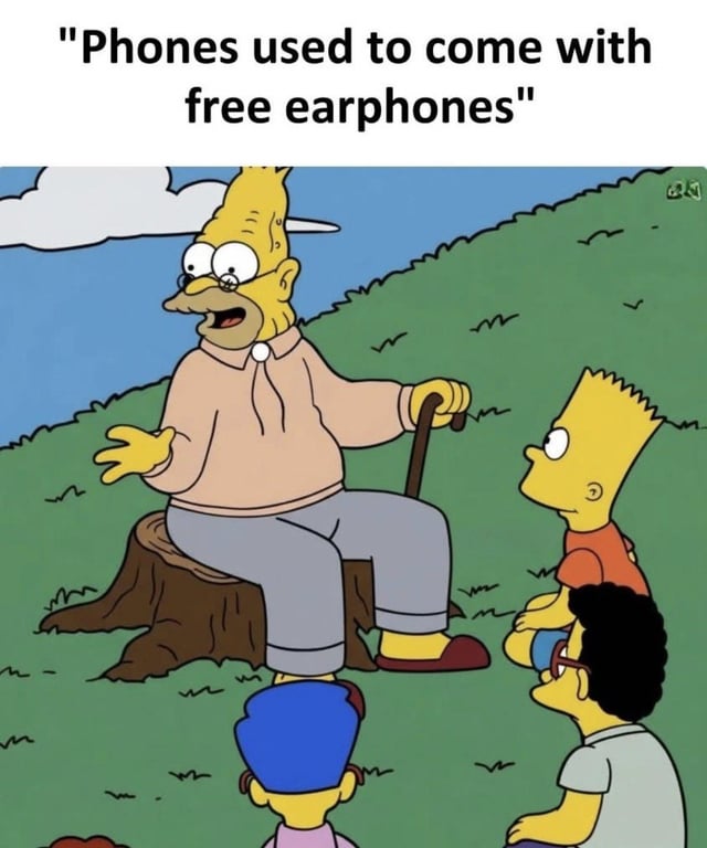 This meme uses a well-known scene from the animated series *The Simpsons*, where elderly Grampa Simpson sits on a tree stump holding a cane and gestures as he tells a story to a group of younger children including Bart Simpson and Milhouse Van Houten, who listen intently. Overlaid text at the top reads 'Phones used to come with free earphones', framing this now obsolete common practice as a distant, ancient historical fact that older generations share with younger people who never experienced it. The joke satirizes modern smartphone manufacturers that stopped including free earphones (and often chargers) with new devices, frequently justifying this cost-cutting move as being for environmental benefit, which aligns with the associated original title that jokes the 'dark ages' began when these changes were framed as environmentally friendly.