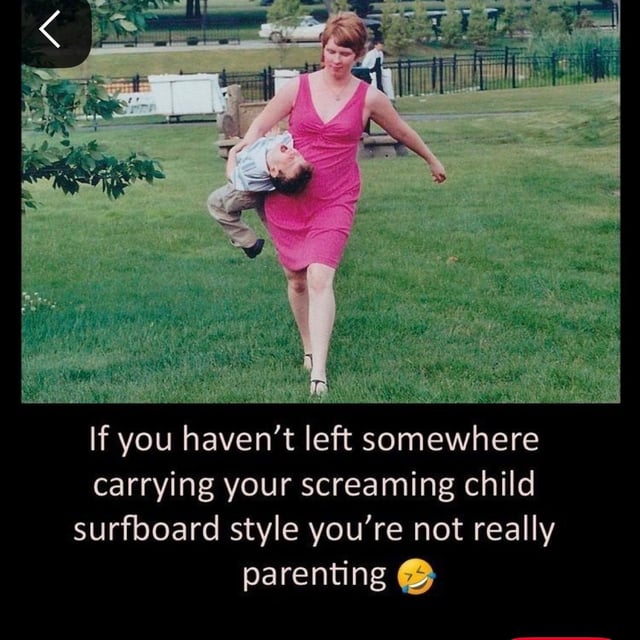 This meme focuses on the relatable chaos of parenting toddlers. The upper section of the image is a candid photograph taken in a public park: a woman wearing a bright pink sleeveless dress walks across a green grass lawn, holding an upset, screaming young toddler horizontally under her arm as if she is carrying a surfboard, with a resigned, tired yet slightly amused expression. Below the photo, white text on a black background reads: 'If you haven’t left somewhere carrying your screaming child surfboard style you’re not really parenting' followed by a laughing crying emoji. The joke frames this messy, often embarrassing experience of having to remove an upset toddler from a public place as a universal, expected part of being a parent to young children.