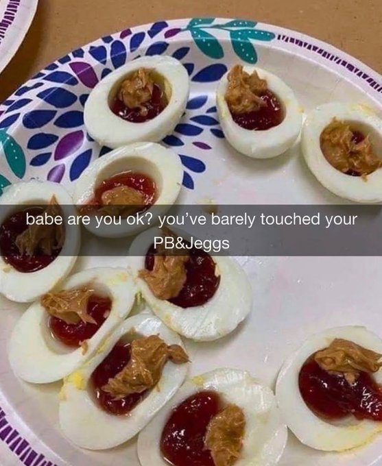 The image displays a disposable paper plate with a blue, purple, and teal leaf pattern holding several halved hard-boiled egg whites. Each egg cup is filled with red fruit jelly and topped with a scoop of peanut butter, creating an extremely unappealing, unusual food combination. Overlaid text uses the popular meme format asking 'babe are you ok? you’ve barely touched your PB&Jeggs'. The core joke is a pun combining the common American food 'PB&J' (peanut butter and jelly sandwich) with 'eggs' to create the portmanteau 'PB&Jeggs', implying the disgusting combination is so unpalatable no one would want to eat it.