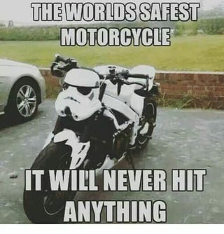 A meme image featuring a motorcycle with a Stormtrooper helmet (from the Star Wars franchise) attached to its front section. The top text overlay reads 'THE WORLD'S SAFEST MOTORCYCLE' and the bottom text states 'IT WILL NEVER HIT ANYTHING'. The humor derives from the pop culture trope that Stormtroopers are notoriously inaccurate marksmen, implying the motorcycle—with a Stormtrooper 'controlling' it—would never hit any objects, thus being 'safe'. The background shows a paved area with a partial view of a silver car and a brick wall with green grass beyond.