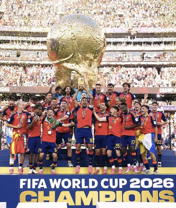 This is a satirical edited photo showing the Spain men's national football team posing on a winner's podium marked with "FIFA WORLD CUP 2026 CHAMPIONS". The team members are wearing their red and blue uniforms and winner's medals, cheering while holding up a small World Cup trophy, with confetti falling and a packed stadium crowd in the background. A disproportionately large World Cup trophy is placed behind the team, where former US president Donald Trump was superimposed in the earlier version of this meme, implying Trump has been digitally removed and replaced with the trophy for comedic effect. The joke references widespread online discourse claiming Trump was edited out of official 2026 FIFA World Cup trophy presentation footage.