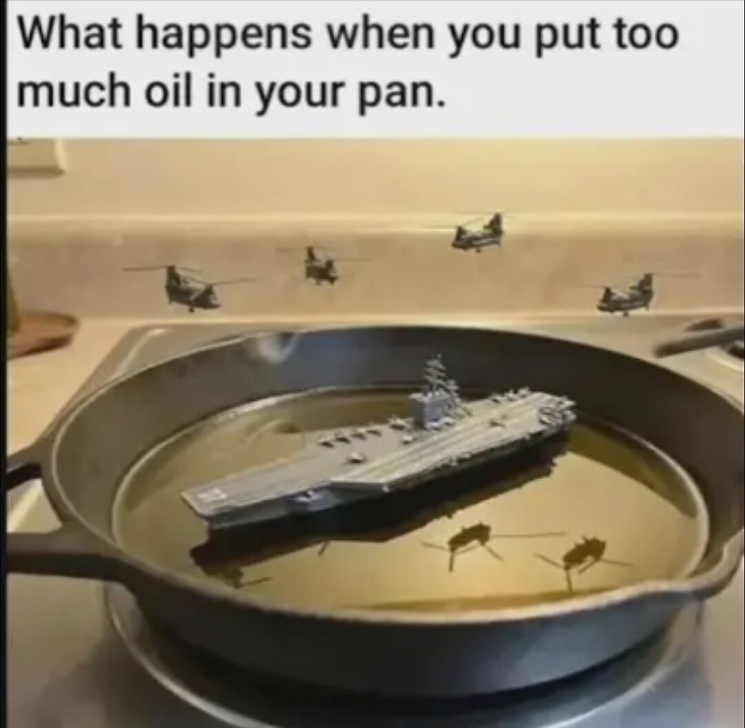 This is an absurdist humorous meme image. The top of the image displays text reading 'What happens when you put too much oil in your pan.' Below the text, a cast iron frying pan sits on a stovetop filled with an excessive amount of cooking oil. A miniature model of a military aircraft carrier is floating in the oil, while edited small military helicopter models appear to be flying above the pan over the kitchen counter, with their reflections visible on the surface of the oil. The joke relies on absurdity, framing the excess cooking oil as a deep enough body of water to support an entire naval carrier strike group, poking fun at the common cooking mistake of using far too much oil when frying.
