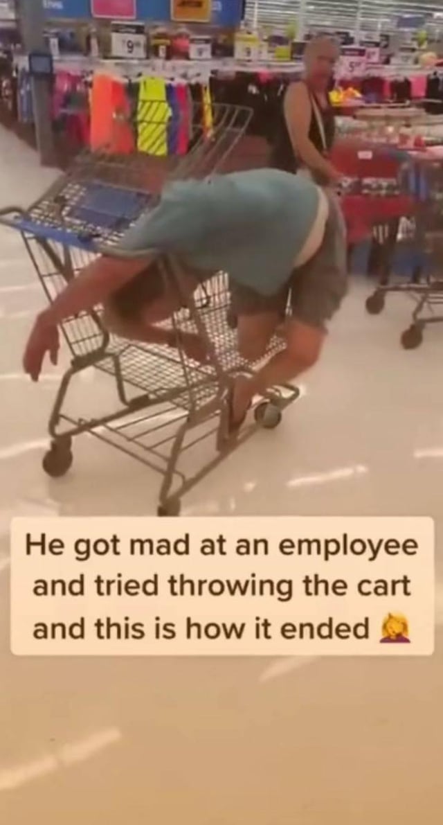 A photograph taken inside a retail store showing a man in a light blue shirt and gray shorts tangled awkwardly in a shopping cart. The man is bent over with his upper body and legs inserted through the cart's metal frame, appearing to have lost balance while attempting to throw or tip the cart. In the background, another individual (likely a store employee) stands near a red cart, observing the scene. Below the image, a caption reads: 'He got mad at an employee and tried throwing the cart and this is how it ended 😂' with a laughing emoji, emphasizing the comedic failure of his angry action.