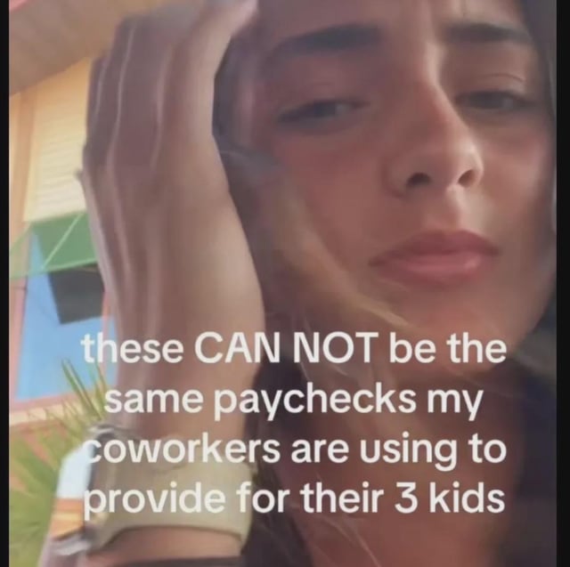 The image is a close-up selfie of a young woman resting one hand on the side of her head, wearing a tired, baffled, disbelieving expression. White overlaid text across the lower half of the image reads: 'these CAN NOT be the same paychecks my coworkers are using to provide for their 3 kids'. The meme expresses a common relatable sentiment among working people: confusion and shock that the same salary they struggle to live on individually is apparently sufficient for their coworkers to support large families, highlighting differing personal financial circumstances, budgeting skill gaps, or perceived wage inadequacy amid rising cost of living.