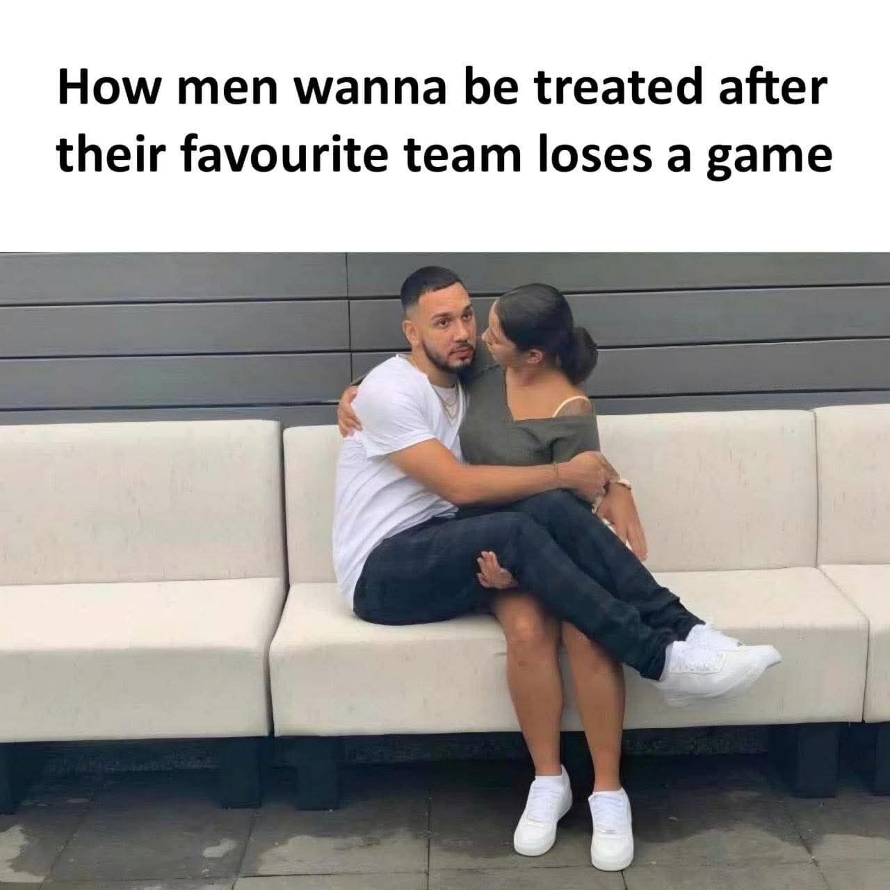 The meme is made up of text placed at the top of a candid photograph of a couple. The top text reads 'How men wanna be treated after their favourite team loses a game'. The photograph shows a man with a disappointed, dejected expression sitting fully on his female partner's lap while she holds him in a warm, comforting embrace and looks at him tenderly. The humor comes from highlighting the underdiscussed desire for men to receive gentle, nurturing comfort when they are upset over small disappointments like their favorite sports team losing a match, which subverts the common gendered expectation that men are always the party providing physical comfort in romantic relationships.