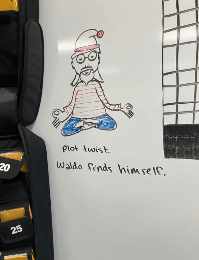 This image shows a hand-drawn marker doodle on a plain whiteboard. The drawing depicts Waldo, the iconic hidden character from the *Where's Waldo?* (also known as *Where's Wally?*) children's book franchise, sitting cross-legged in a peaceful lotus meditation pose with his eyes closed, hands held in meditation mudras. He is drawn wearing his signature red-and-white striped shirt, blue trousers, round glasses, goatee, and signature white hat with a red brim and red pompom. Below the drawing, handwritten black text reads: 'plot twist. Waldo finds himself.' To the left of the whiteboard, padded sports gear bags marked with the numbers 20 and 25 are partially visible, while a metal wire rack is partially seen on the right. The joke subverts the core premise of the *Where's Waldo?* franchise, where audiences actively search for the hidden Waldo in crowded illustrations, by framing Waldo as having achieved self-realization through meditation, so he no longer needs to be found by others.