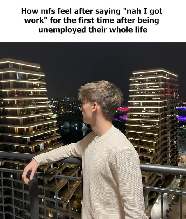 A meme featuring a photograph of a young man standing on a balcony at night, gazing at a cityscape with illuminated high-rise buildings. The top of the image displays a humorous caption: 'How mfs feel after saying 'nah I got work' for the first time after being unemployed their whole life'. The man's contemplative posture and the scenic urban backdrop humorously capture the mix of pride and reflection associated with transitioning from long-term unemployment to having a job.
