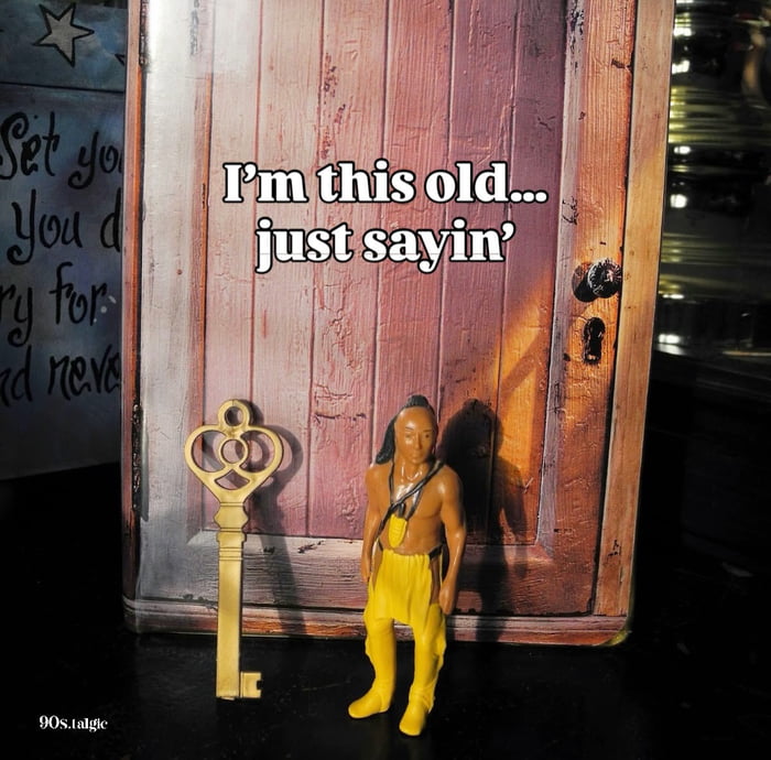 The image displays a small plastic toy figure of the character Little Bear from *The Indian in the Cupboard*, standing beside a large vintage-style skeleton key, positioned in front of a printed backdrop of a worn wooden cupboard door. Bold white overlaid text reads 'I'm this old... just sayin''. The meme is a nostalgic joke: people who recognize the characters and plot of the 1995 family film *The Indian in the Cupboard* (where a magic key brings toy figures to life when used on a special cupboard) understand that the poster is indicating they are old enough to have grown up with the film or its associated merchandise from the 1990s. A watermark reading '90s.talgic' is visible in the bottom left corner.