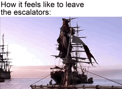 The meme has top text that reads 'How it feels like to leave the escalators:' placed above a still from the Pirates of the Caribbean film franchise, where Captain Jack Sparrow stands dramatically and triumphantly at the top of his pirate ship's mast overlooking the ocean as if he has just completed an epic, high-stakes voyage. The core joke relies on absurd exaggeration: the extremely mundane, trivial action of stepping off an escalator is compared to a grand, legendary victory, resonating with audiences that feel a small, silly sense of accomplishment after completing minor everyday tasks.
