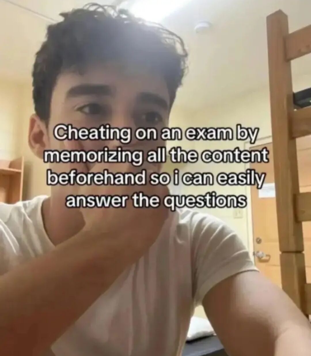 This is a relatable humorous meme featuring a young man in a dorm room environment, holding his hand up to his mouth in a mischievous, scheming expression as if sharing a secret trick. Overlaid on the image is text that jokes that 'cheating on an exam by memorizing all the content beforehand so I can easily answer the questions' is a clever cheat method. The joke relies on irony, as memorizing content to take an exam is the standard, acceptable way to prepare, not actual cheating, so framing legitimate studying as a sneaky hack is played for laughs, resonating with students who find studying for exams tedious.