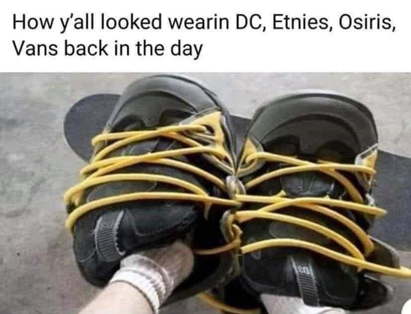 The meme consists of text at the top and a photo below. The top text reads "How y'all looked wearin DC, Etnies, Osiris, Vans back in the day". The photo shows a person wearing white socks standing on a skateboard, with a pair of oversized black skate shoes with extra long yellow laces arranged facing forward. The shoe tongues look like wide eyes, and the crisscrossed yellow laces look like jagged teeth, making the pair of shoes look like a goofy, wide-mouthed cartoon face. The joke pokes fun at the extremely bulky, oversized silhouette of popular skate shoe brands from the 1990s and 2000s, implying the shoes looked so awkwardly large that people wearing them resembled this silly face made from tied shoes.