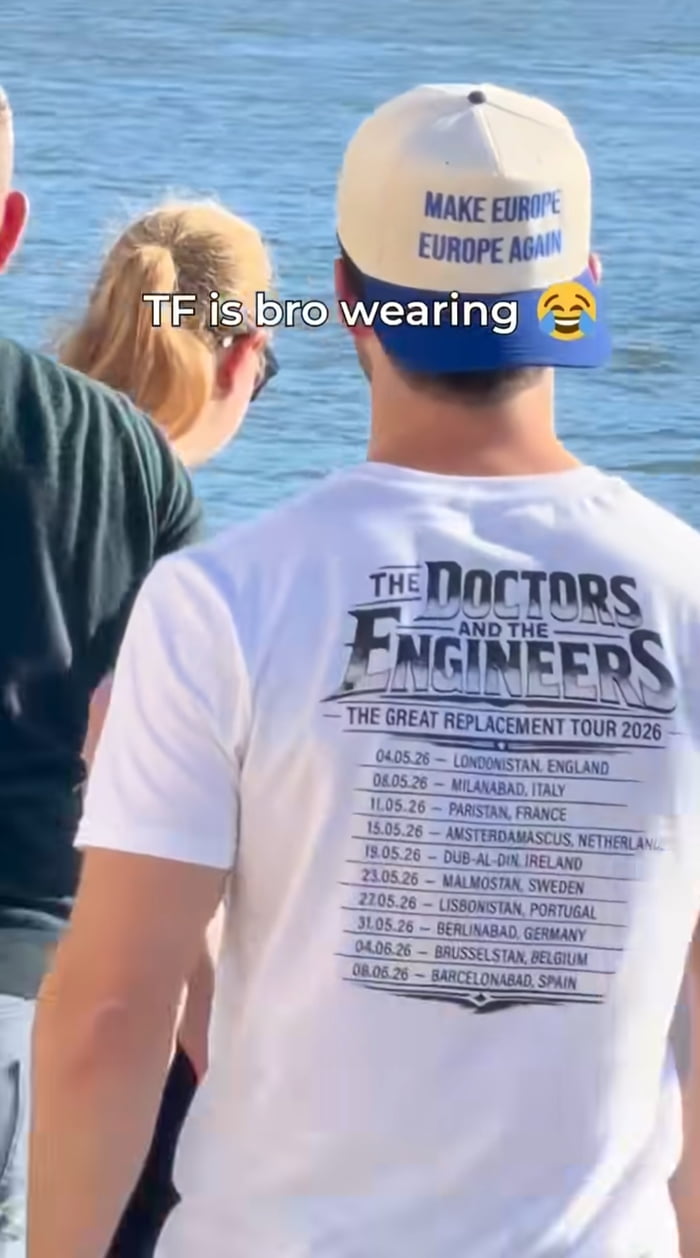 The image shows a rear view of a man standing near a body of water, next to two other people (one man in a dark shirt on the left, one blonde woman with a ponytail in front of him). The man wears a two-tone cream and blue baseball cap worn backwards, printed with the text 'MAKE EUROPE EUROPE AGAIN' -- a parody of the American 'Make America Great Again' political slogan, tied to anti-immigration far-right ideology. His white t-shirt is designed in the style of a band tour shirt, printed on the back with: 'THE DOCTORS AND THE ENGINEERS / THE GREAT REPLACEMENT TOUR 2026', followed by a list of European city names altered to add Arabic/Muslim naming conventions (e.g. Londonistan for London, Parisistan for Paris, Berlinabad for Berlin). These altered names reference the debunked far-right 'Great Replacement' conspiracy theory that claims white European populations are being systematically replaced by Muslim and non-white immigrants. Overlaid on the upper part of the image is reaction text that reads 'TF is bro wearing 😂', expressing shocked, amused disbelief at the offensive and absurd clothing the man is wearing.
