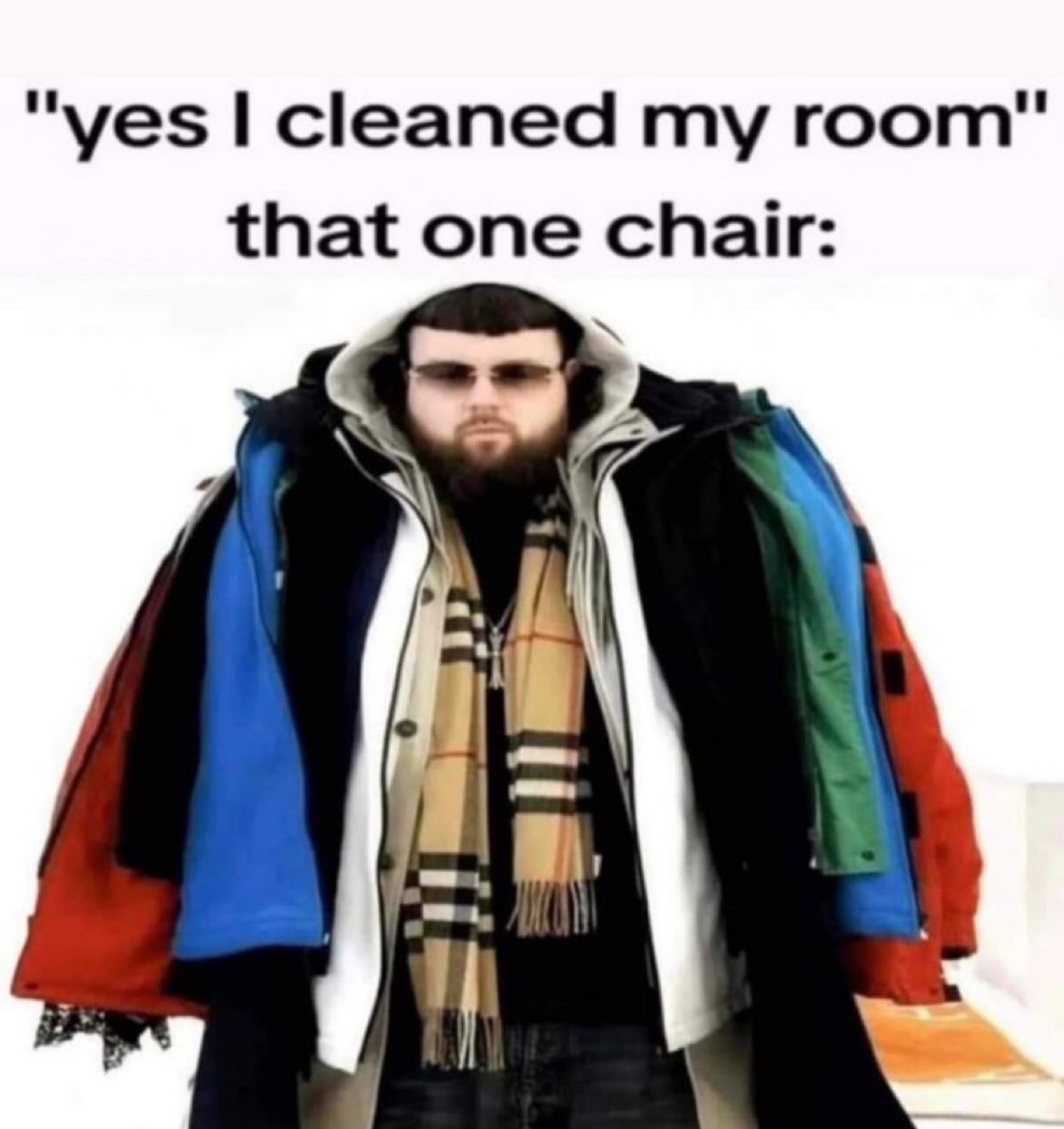 The meme displays text at the top reading "yes I cleaned my room" that one chair:, followed by a photograph of a bearded man in sunglasses wearing an absurd number of layered, multi-colored winter jackets (red, blue, white, black, green) alongside a Burberry checkered scarf. The joke is a widely relatable reference to the common household habit of piling all loose clothing onto a single chair instead of putting items away during surface-level room cleaning, with the over-layered man acting as a visual metaphor for the clothing-covered chair.