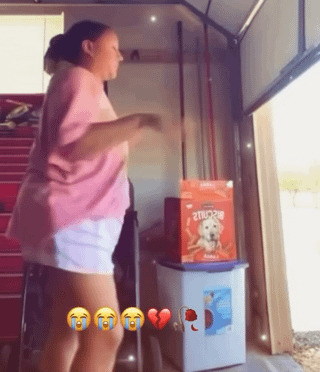 A meme image depicting a real woman in a garage or storage area, captured mid-action with an energetic posture, possibly dancing or gesturing dynamically. She is wearing a pink shirt and white shorts. In the background, there is a red box labeled 'Zuke's' (likely dog food) placed on top of a blue container. At the bottom of the image, the emojis 😂😂😂❤️🔥 are overlaid, conveying amusement and excitement. The scene appears casual and unscripted, emphasizing a lighthearted, chaotic vibe.