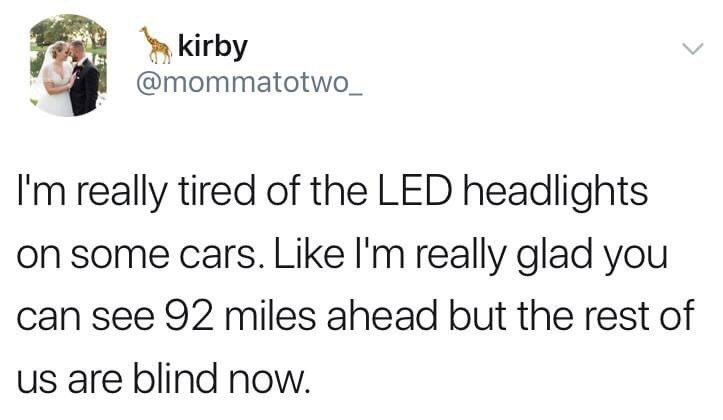 This image is a screenshot of a public post from X (formerly Twitter). The post is made by user with display name 'kirby' and handle @mommatotwo_, whose profile picture shows a bride and groom posing happily for a wedding photo, with a giraffe emoji next to the display name. The post text humorously and sarcastically complains about the excessive brightness of LED headlights installed on some modern cars: it jokes that while the driver using these LED lights can see as far as 92 miles ahead, all other nearby drivers are temporarily blinded by the harsh, intense light, a common frustration shared by many drivers.