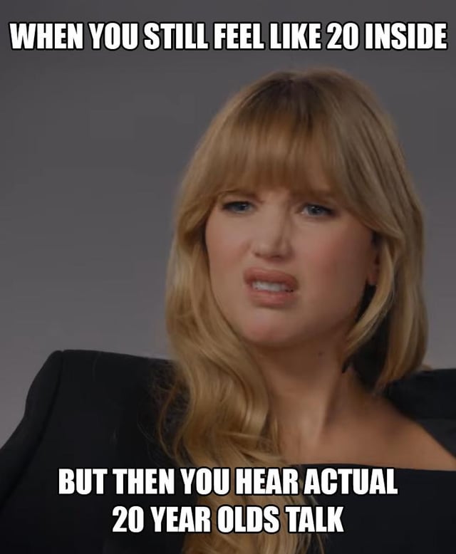 The image features a woman with long, wavy blonde hair and bangs, wearing a black outfit, set against a plain gray background. She has a neutral-to-slightly-confused expression, with her head tilted slightly to the side. Overlaid text appears at the top and bottom of the image: the top text reads 'WHEN YOU STILL FEEL LIKE 20 INSIDE' and the bottom text reads 'BUT THEN YOU HEAR ACTUAL 20 YEAR OLDS TALK'. The meme humorously contrasts the internal feeling of being 20 with the reality of hearing current 20-year-olds speak, highlighting a relatable generational or age-related disconnect.
