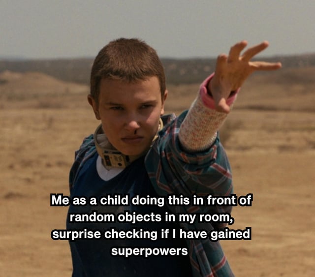 The image features Eleven, a character from the TV series 'Stranger Things', in a desert-like environment. She has a focused and determined expression, extending her right hand forward in her iconic telekinetic gesture. Overlaid on the image is a humorous caption: 'Me as a child doing this in front of random objects in my room, surprise checking if I have gained superpowers'. The meme playfully connects the universal childhood fantasy of discovering superpowers to Eleven's signature ability from the show, creating a relatable and nostalgic humor element.
