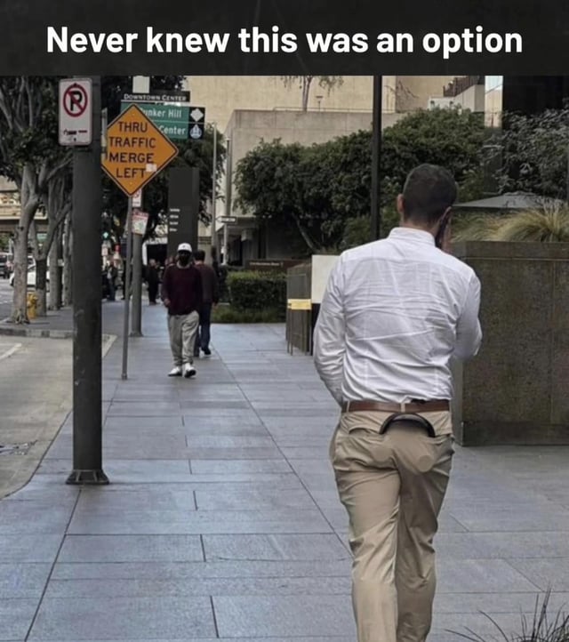 A photograph of a man walking on a city sidewalk, viewed from behind. He is wearing a white button-up shirt and beige pants, with a noticeable holster attached to his belt. The top of the image displays the text 'Never knew this was an option' in bold white letters. In the background, there are other pedestrians walking, trees, and street signs including a 'NO PARKING' sign and a yellow 'THRU TRAFFIC MERGE LEFT' sign. The scene appears to be in an urban area with buildings and greenery lining the street.