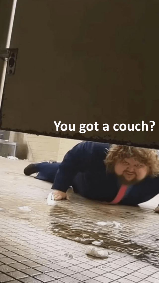 A meme image depicting a person with curly hair wearing a blue suit and red tie lying on a wet, debris-strewn tiled floor beneath a large object (possibly a door or heavy furniture). The individual appears to be crawling or reaching out with an intense, urgent expression. Prominent overlaid text at the top of the image reads 'You got a couch?'