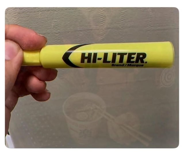 The image displays a close-up shot of a person's hand holding a standard bright yellow HI-LITER brand highlighter against a plain grey textured background. The core joke of the meme, paired with its title, references the common relatable experience of misreading ordinary words when very sleep-deprived late at night: the brand name "HI-LITER" can easily be misread as the far more shocking term "HITLER" when one is tired and not reading carefully at 2am, creating a sudden, funny moment of alarm before the viewer realizes it is just a standard highlighter brand name.