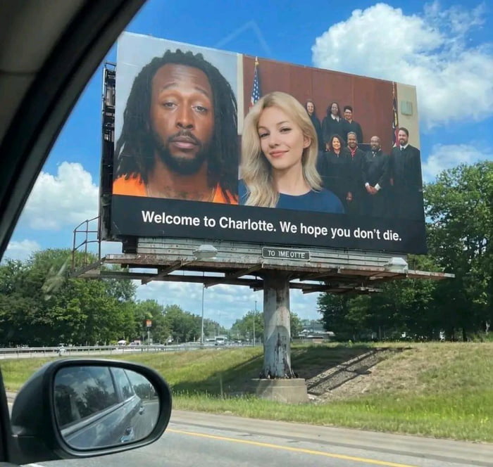 This image is a first-person view from inside a car driving on a highway, looking out at a large roadside billboard that has been digitally edited for comedic effect. The billboard displays three images side-by-side: on the left is a public mugshot of a Black man in an orange correctional jumpsuit, in the center is a headshot of a smiling blonde woman, and on the right is an official group photo of multiple judges wearing judicial robes with an American flag in the background. Below the images, large white text on a black background reads 'Welcome to Charlotte. We hope you don't die.' The joke relies on public discourse around high profile violent crime cases and widespread criticism of the Charlotte, North Carolina justice system for perceived leniency on violent offenders and unfair rulings, sarcastically implying that visitors to the city face high risk of harm.