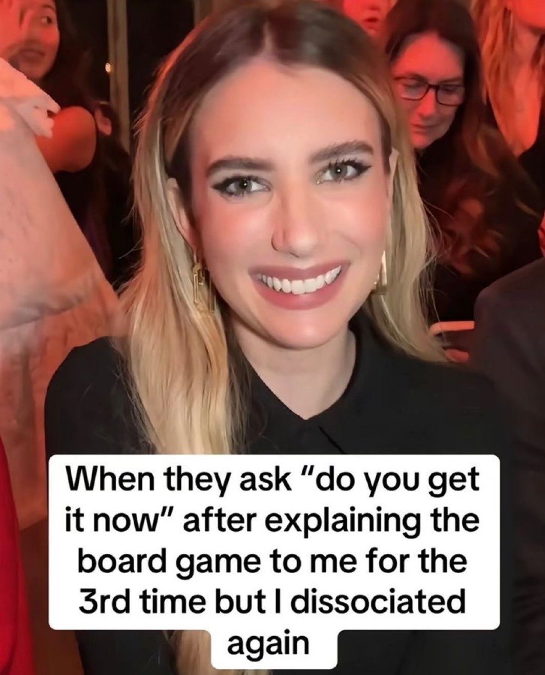 This reaction meme features a photo of actress Emma Roberts sitting in a public event audience, displaying a wide, forced, overly polite smile that appears to mask internal confusion or disinterest. A text overlay is placed at the bottom of the image describing a relatable scenario: being asked if you understand board game rules after three explanations, even though you zoned out and dissociated again instead of listening. The humor comes from how perfectly Emma's forced smile captures the feeling of pretending to understand something to avoid burdening someone with repeating an explanation, even when you have no idea what they are talking about.