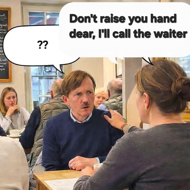 This is a single-panel speech bubble meme set in a casual cafe. A middle-aged man with a confused, bewildered expression sits across a wooden table from a woman whose back faces the viewer, with her hand resting on the man's shoulder. The woman's speech bubble reads 'Don't raise you hand dear, I'll call the waiter' (containing a common typo where 'your' is written as 'you'), while the man's speech bubble only contains '??', indicating he had no intention of calling a waiter and is confused by the woman's statement. The joke rests on the woman completely misinterpreting the man's intended action, paired with the original title 'He still doesn't get it' which implies the man is unaware of whatever action the woman thought he was about to take. Other cafe patrons are visible in the background, along with a chalkboard menu on the left wall.