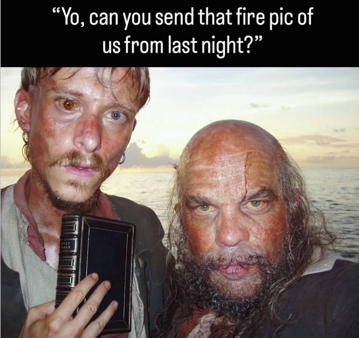 The image features two weathered-looking men standing at the ocean's edge during sunset. Both have sunburned skin and intense expressions. One man has a beard and is holding what appears to be a book or Bible. The top of the image contains overlaid text that reads: "Yo, can you send that fire pic of us from last night?" The contrast between the men's rugged appearance and the casual request for a "fire pic" (slang for an impressive photo) creates an ironic and humorous effect.