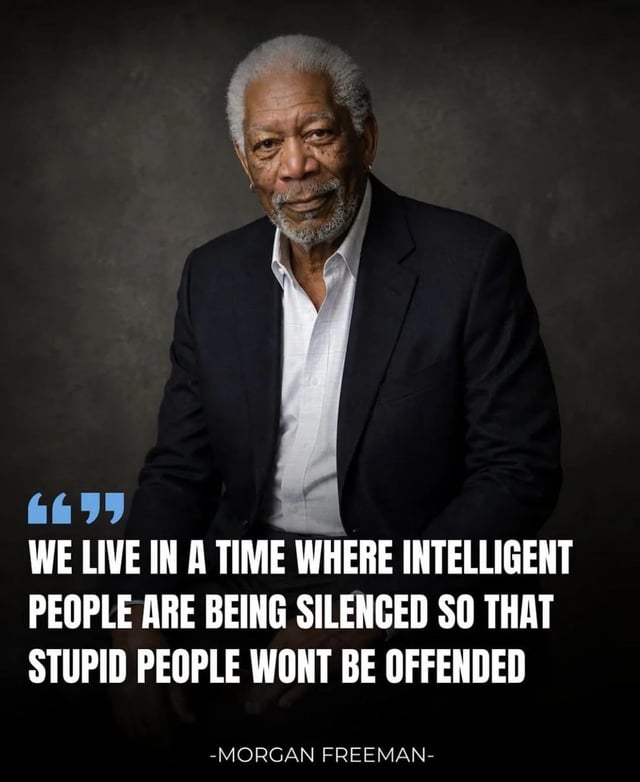 This is a single-image meme featuring a professional upper-body portrait of acclaimed actor Morgan Freeman. He is wearing a dark navy blazer over an unbuttoned white dress shirt, with a calm, gentle smile, facing the viewer against a muted dark grey studio background. Below the portrait, large bold white text displays a quote: "WE LIVE IN A TIME WHERE INTELLIGENT PEOPLE ARE BEING SILENCED SO THAT STUPID PEOPLE WONT BE OFFENDED", with light blue opening quotation marks to the left of the text, and the text "-MORGAN FREEMAN-" centered below the quote as attribution. The meme is intended to convey agreement with the sentiment that thoughtful, critical voices are culturally suppressed to avoid offending people with less informed opinions, despite the quote being falsely attributed to Freeman.